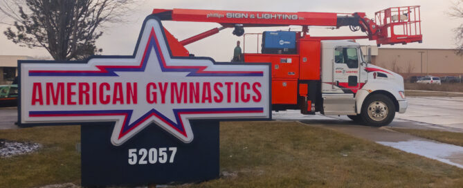 American Gymnastics illuminated monument sign with Phillips Sign & Lighting company in Michigan with orange service truck in the background.