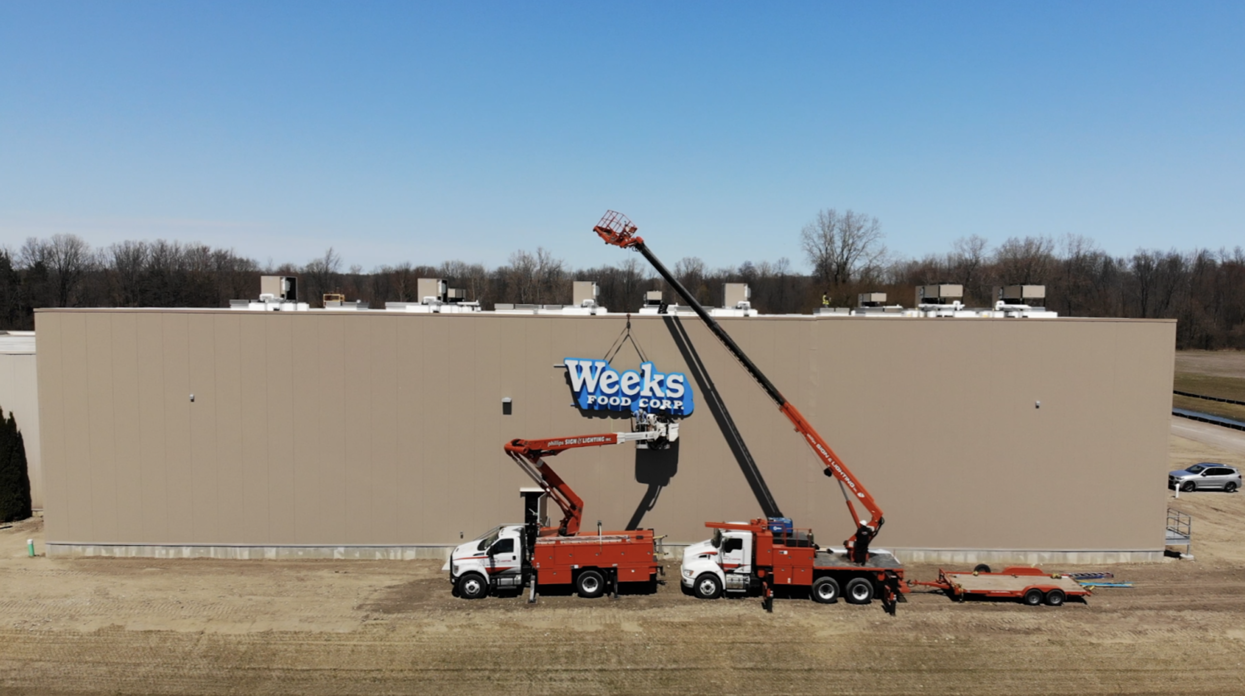 Wide aerial view of the Weeks Food Corp. 50,000 square foot building expansion with two red crane trucks installing the blue and white wall sign.